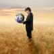 A person holding on the globe in his hands while standing in fields.