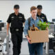 AI-generated image, by Z-Image vanilla, running on Krita AI Diffusion: 'An office full of robots, and a young worker (a white male) is being escorted out by two security guards, carrying his box of possessions from his vacated desk, including a plant'