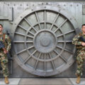 Imagen generada por IA, Z-Image Turbo vía Krita Diffusion AI + Photoshop 2023 (sin IA): «Interior. Foto de dos corpulentos guardias militares estadounidenses, de guardia con grandes rifles automáticos, frente a la enorme y compleja puerta de la bóveda de un banco. Imagen de archivo. La puerta de la bóveda es de acero grueso y parece impenetrable».