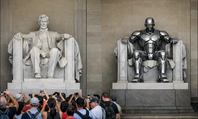 An AI-generated photo of the Abraham Lincoln memorial thronged with tourists, next to a copy of the seated Lincoln statue, which has been substituted by a shiny robot. The robot has no tourists at its feet. Model: GPT-1.5.