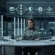 A cinematic, wide-angle shot of a technical professional sitting at a futuristic curved workstation in a dark data center, orchestrating a complex digital workflow displayed on glowing holographic glass panels.