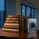A row of antique leather-bound books stands next to a glowing metal bookend featuring a purple light-up geometric structure on a wooden desk in a modern high-rise office at night.