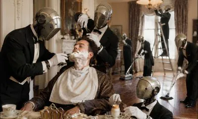 AI-generated image (GPT-2): A man sits at breakfast while a group of identical domestic robots shave him, cut his hair, prepare his food, and clean the house around him, turning even the smallest daily tasks into outsourced labor.