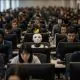 AI-generated image (GPT-2): Rows of human workers focus on their computer screens while a distracted robot, seated among them, tries to look up at a yellow canary perched on its head.