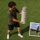 AI-generated image (GPT-2 + Photoshop): High-angle view of a man holding a scale model of the Leaning Tower of Pisa on a grassy field, with an inset photograph showing the same model aligned from ground level to resemble the full-sized tower in the background.