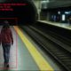 AI-generated image (GPT-2): A surveillance-style view of a subway platform showing a person walking near the platform edge, with an AI monitoring overlay displaying a detection box around the individual, a tunnel entrance ahead, and passengers visible on the opposite platform.