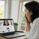 A woman looks at a laptop displaying a news website, reacting with surprise as a banner advertisement on the page shows a smiling woman who closely resembles her.