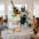 AI-generated image (GPT-2): an industrial humanoid robot stands beside a restaurant birthday table, holding a running chainsaw near a lit cake while surrounding diners react with visible alarm.