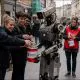 AI-generated image (GPT-2) - An industrial humanoid robot holds a Save the Children donation tin on a British high street as several passers-by place five pound notes into it, while nearby human volunteers in red Save the Children vests stand with their own collection tins and watch with puzzled expressions.