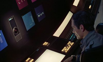 David Bowman (Keir Dullea) sits at a dark control console, speaking with super-computer HAL 9000, surrounded by illuminated panels, amber buttons, blue displays and rectangular light panels, in Stanley Kubrick's '2001: A Space Odyssey' (1968). Credit: MGM/Allstar