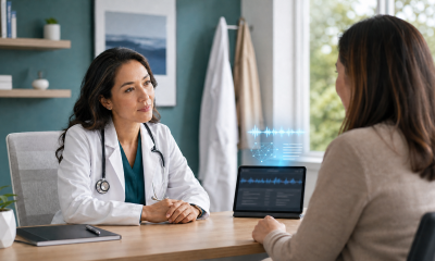 Physician speaking with a patient as an AI medical scribe visualizes audio and draft notes above a tablet