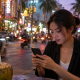 Woman using a smartphone at an outdoor café, with the screen facing her.