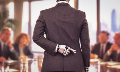 GPT Image 2 (AI-generated image): A humanoid robot wearing a dark suit stands with its back to the camera at a conference table, with one mechanical hand with fingers crossed behind its back. Blurred business attendees sit on both sides, with papers, glasses, windows, and a city view in the background.