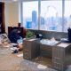 AI-generated image: three police officers examine a ransacked high-rise office. One takes notes beside a bookcase, another crouches among scattered papers and broken glass, and a third stands by a sofa. An overturned desk and fallen plants occupy the foreground. A large jagged hole punctures a window overlooking city skyscrapers. Image generated by ChatGPT Images 2.5 and tweaked in Photoshop 2023.