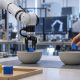 Robot arm placing a block into a bowl beside a human hand demonstrating the task
