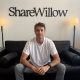 ShareWillow founder and CEO Ryan Shank seated beneath the company sign.